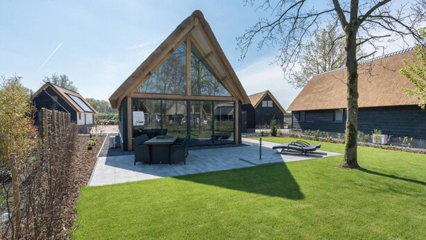 Une maison moderne dotée d’une grande véranda en verre, d’un toit de chaume et d’une pelouse bien entretenue.