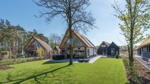 Une maison moderne dotée d’une grande véranda en verre, d’une pelouse bien entretenue et d’un mur en pierre.
