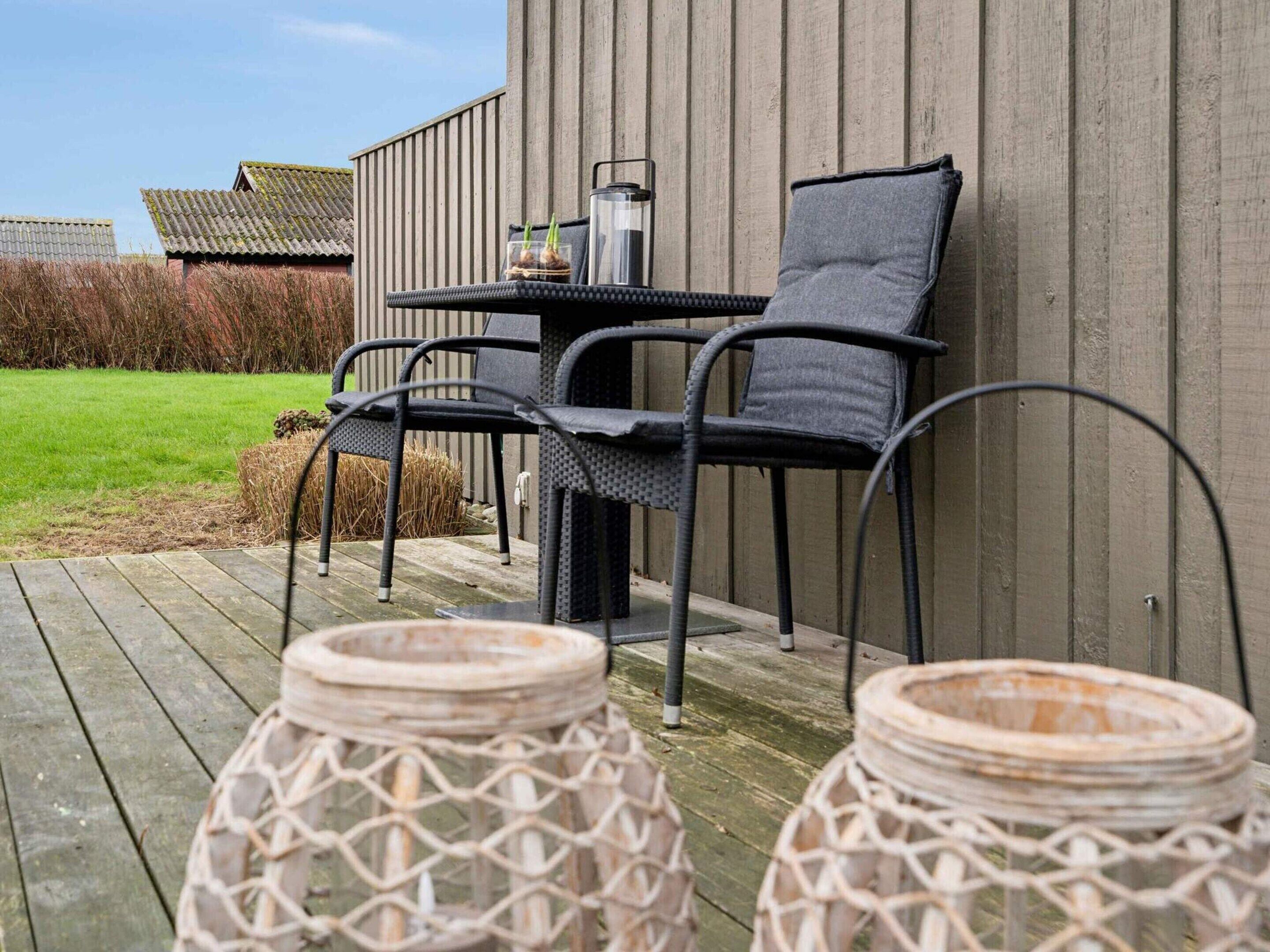 Een terras met een tafel en stoelen, een houten terras en twee rieten lantaarns.