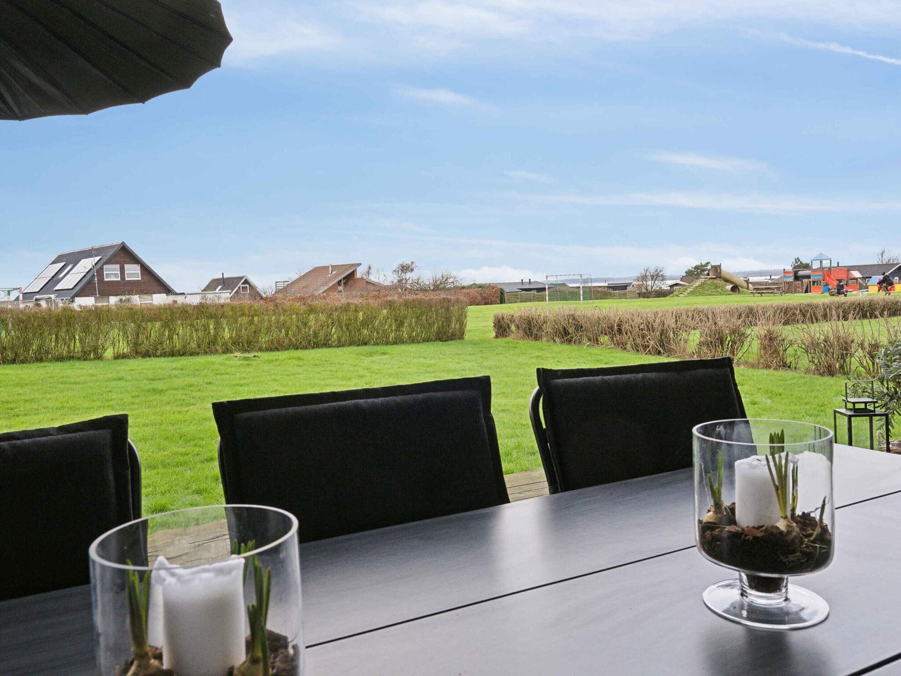 Ein Tisch mit Stühlen und einem Glas Wasser, mit Blick auf ein Wiesenfeld und Häuser.
