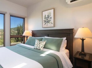 A bed with a green bedspread and pillows, a framed plant on the wall, and two bedside lamps.