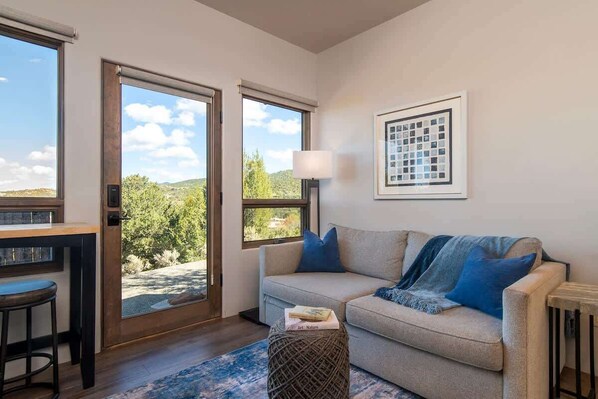 A modern living room with a sofa, a small table, and a view through large windows.