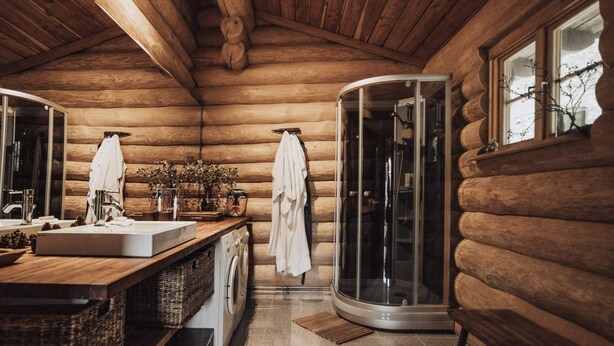 A log cabin bathroom with a wooden interior, a glass-enclosed shower, a sink with a mirror, and a washing machine. - 5 Star Holiday Home in Jaegerspris (Jægerspris)