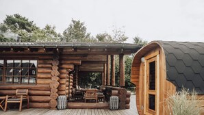 A log cabin with a wooden deck, a dining area with chairs and a table, and a large window overlooking the landscape. - 5 Star Holiday Home in Jaegerspris (Jægerspris)