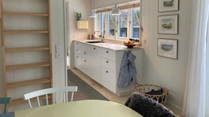 A kitchen with a wooden ladder, white cabinets, a window with a view, and a basket on the floor. - 5 Star Holiday Home in Vejby (Vejby)
