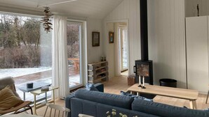A cozy living room with a large blue sofa, a wooden table, and a black wood stove. - 5 Star Holiday Home in Vejby (Vejby)