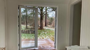 A room with a sliding glass door leading to a wooden deck with a stone wall and trees. - 5 Star Holiday Home in Vejby (Vejby)