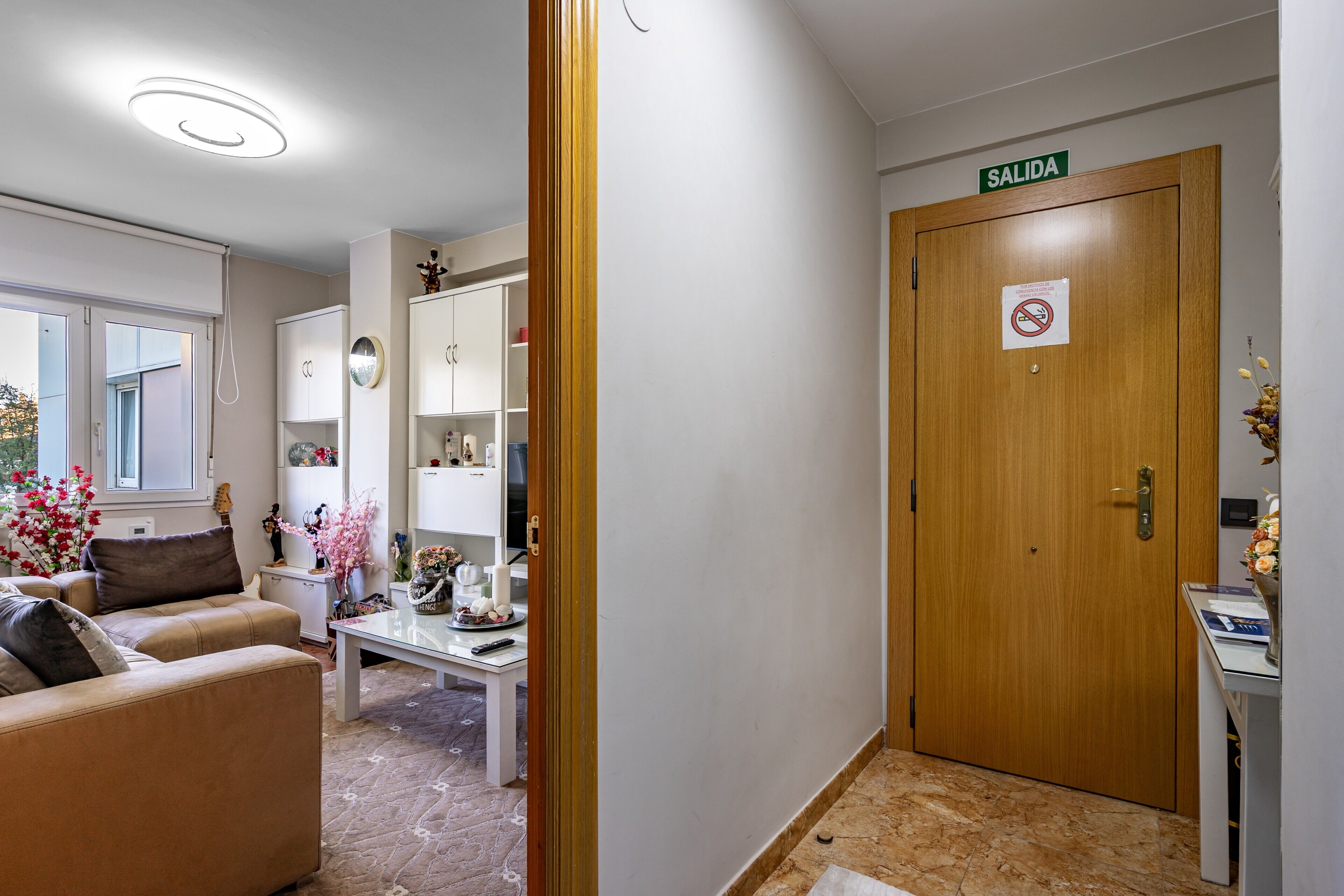 Een hotel lobby met een houten deur waarop 'SALIDA' staat, een bank, een bijzettafeltje en een klein tafeltje met decoratieve objecten.