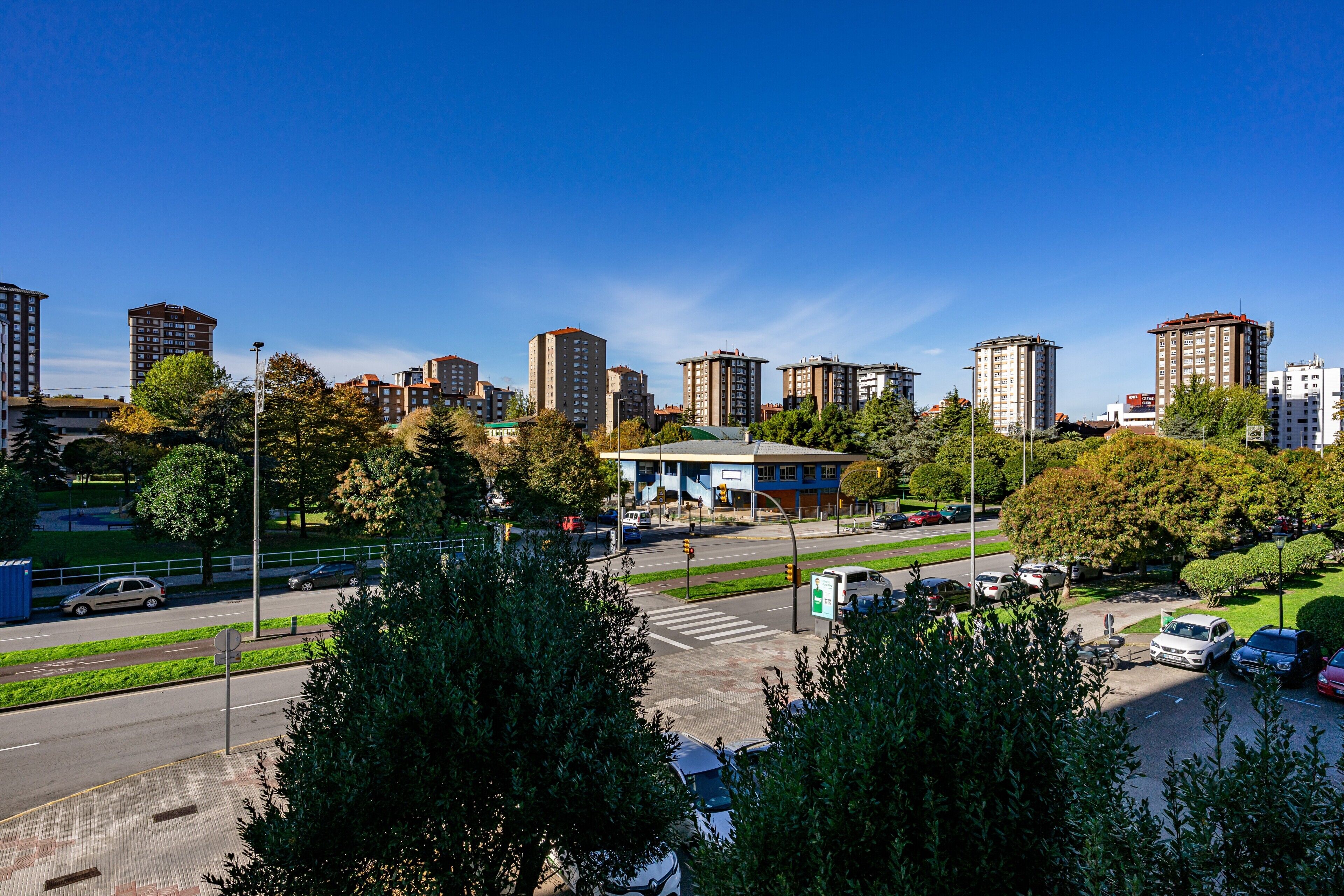 A cityscape with high-rise buildings, a pedestrian crossing, and a parking area.