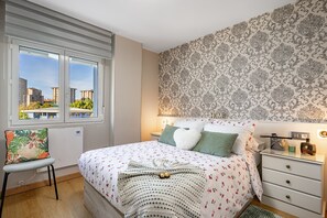 A bedroom with a bed, a chair, a nightstand, and a window with a view of buildings. - 'Rincón De Julia' Apartment with Wi-Fi in Gijón (Gijón)