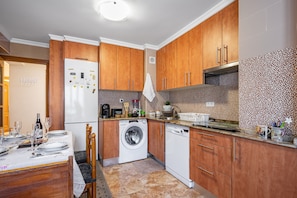 A compact kitchen with wooden cabinets, a washing machine, and a dining area with a table set for two.