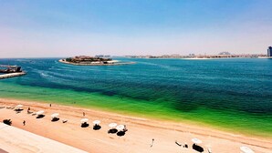 Een strand met helderblauw water, een zandstrand en enkele parasols.