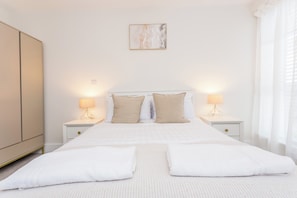 Een slaapkamer met een groot bed, twee nachtkastjes met lampen, een garderobe en een schilderij aan de muur.