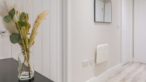 Une salle de bain avec un vase en verre contenant des plantes séchées, posé sur un comptoir noir, un porte-serviettes blanc et un miroir au mur.