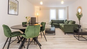 Un salon moderne avec un canapé vert, une table à manger entourée de chaises vertes et un tableau encadré accroché au mur.
