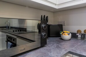 Eine moderne Küche mit Glasküchenrückwand, einer schwarzen Dunstabzugshaube und einer weißen Schüssel mit Besteck auf der Arbeitsplatte.