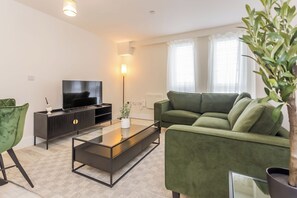 Un salon moderne avec un canapé, une table basse, un téléviseur et une lampe sur pied.