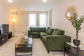 Un salon moderne avec un canapé d’angle, une table basse en verre, un téléviseur et une plante en pot.