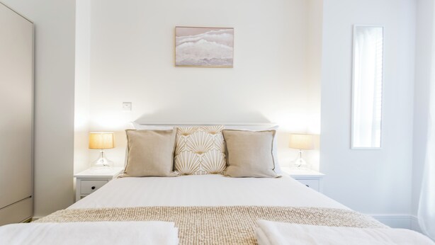 Une chambre à coucher bien rangée, avec un grand lit, deux lampes de chevet, un coussin décoratif et un tableau encadré au mur.