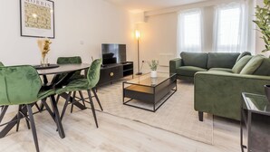 Un salon moderne avec un canapé vert, une table basse en verre et un coin repas avec des chaises vertes.