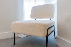 Une chaise dotée d’un siège et d’un dossier moelleux, placée près d’une fenêtre ornée de rideaux légers.