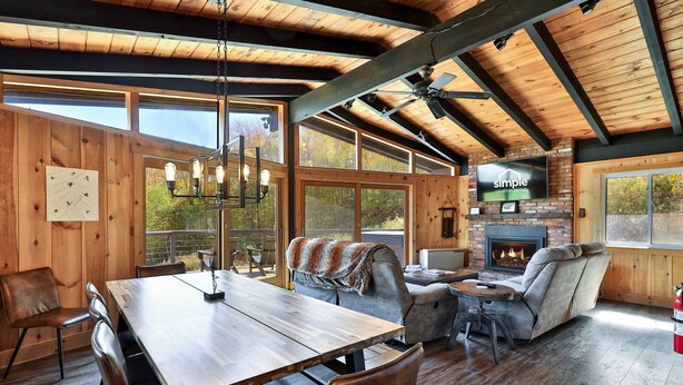 A spacious living area with a wooden ceiling, a fireplace, and a television mounted on the wall. - RoundTop Chalet | Hot Tub, Fire Pit & Mountain Views near Killington & Okemo (Plymouth)