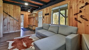 A cozy cabin interior with a gray sectional sofa, a wooden ceiling, and a large window. - RoundTop Chalet | Hot Tub, Fire Pit & Mountain Views near Killington & Okemo (Plymouth)