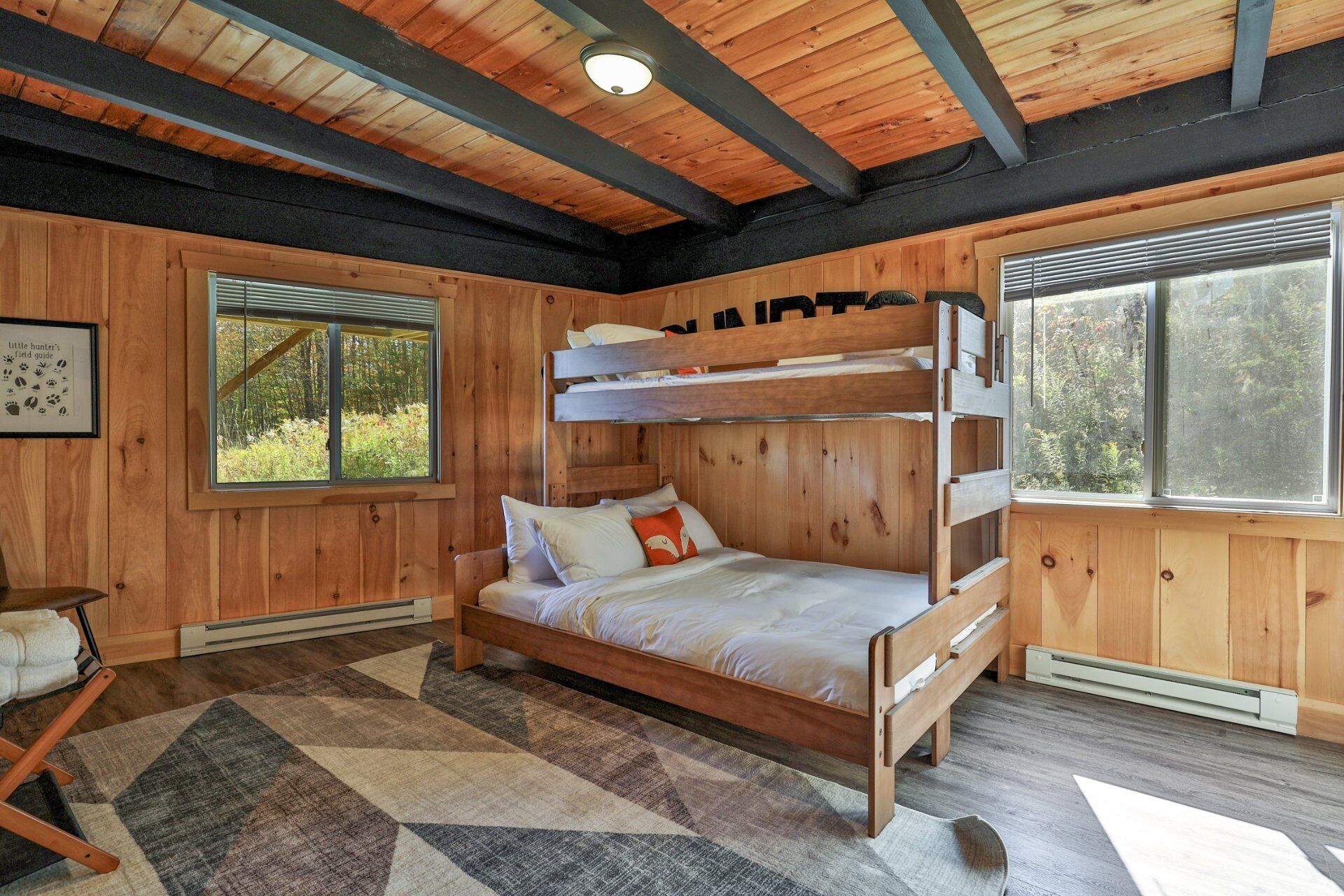 A bunk bed room with wooden walls, a window with blinds, a framed picture, and a rug.