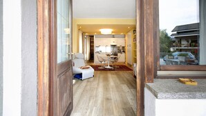 A hallway leading to a dining area with a table and chairs, a kitchen in the background, and a view of a traditional building outside. - Apartment 'Bilocale 10' with Mountain View, Balcony and Wi-Fi (Gressan)