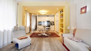 A modern living room with a sofa, a chair, a dining table with chairs, a kitchen in the background, and a bookshelf. - Apartment 'Bilocale 10' with Mountain View, Balcony and Wi-Fi (Gressan)