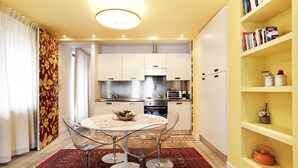 A compact kitchen with modern appliances, a dining area with a round table and chairs, and a bookshelf with books and decorative items. - Apartment 'Bilocale 10' with Mountain View, Balcony and Wi-Fi (Gressan)
