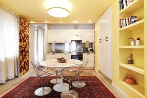 A compact kitchen with modern appliances, a dining area with a round table and chairs, and a bookshelf with books and decorative items.