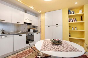 A modern kitchen with white cabinets, a stainless steel range, and a glass dining table with a patterned table runner.