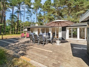 Una moderna veranda esterna con tavolo e sedie, un ombrellone grande e un patio che conduce a un edificio con porte vetrate.