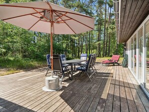 Un terrazzo in legno con tavolo e sedie, un ombrellone e una zona vetrata.