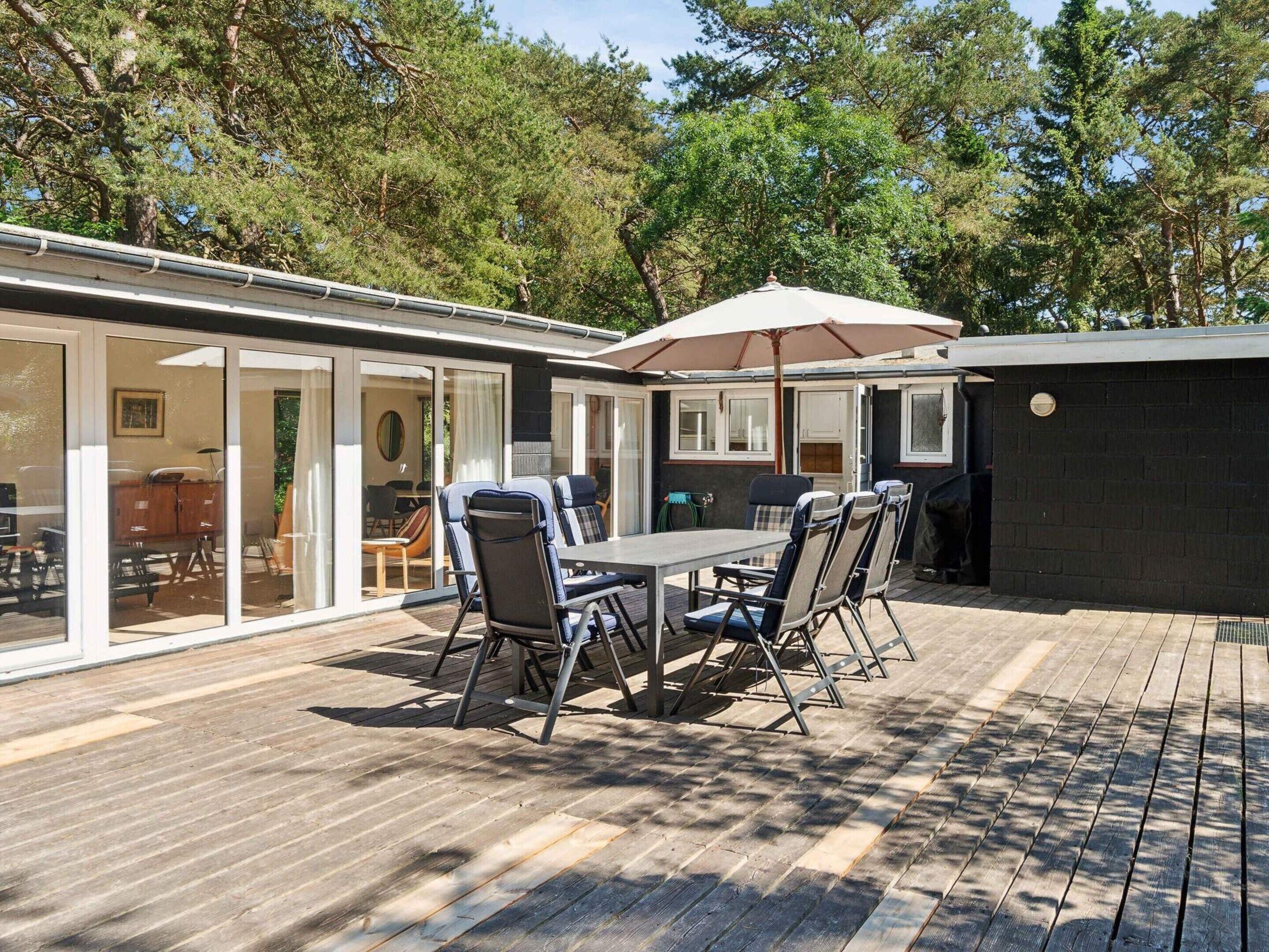 A patio with a table and chairs, a grill, and a covered area with a view of the surrounding trees.