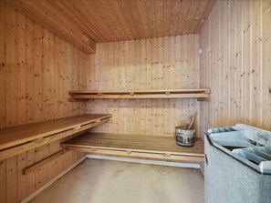 Una sauna con pareti e panche in legno, una panca in pietra e un catino con un cucchiaio di legno.
