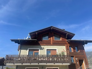 Un bâtiment à deux étages doté d’une façade en bois, d’un balcon orné de balustrades décoratives et, en arrière-plan, d’un ciel d’un bleu éclatant.