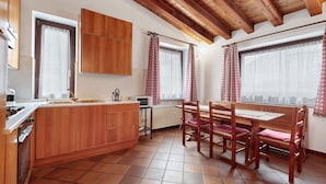 Una cocina con armarios de madera, una mesa de comedor con sillas y un ventanal con cortinas.