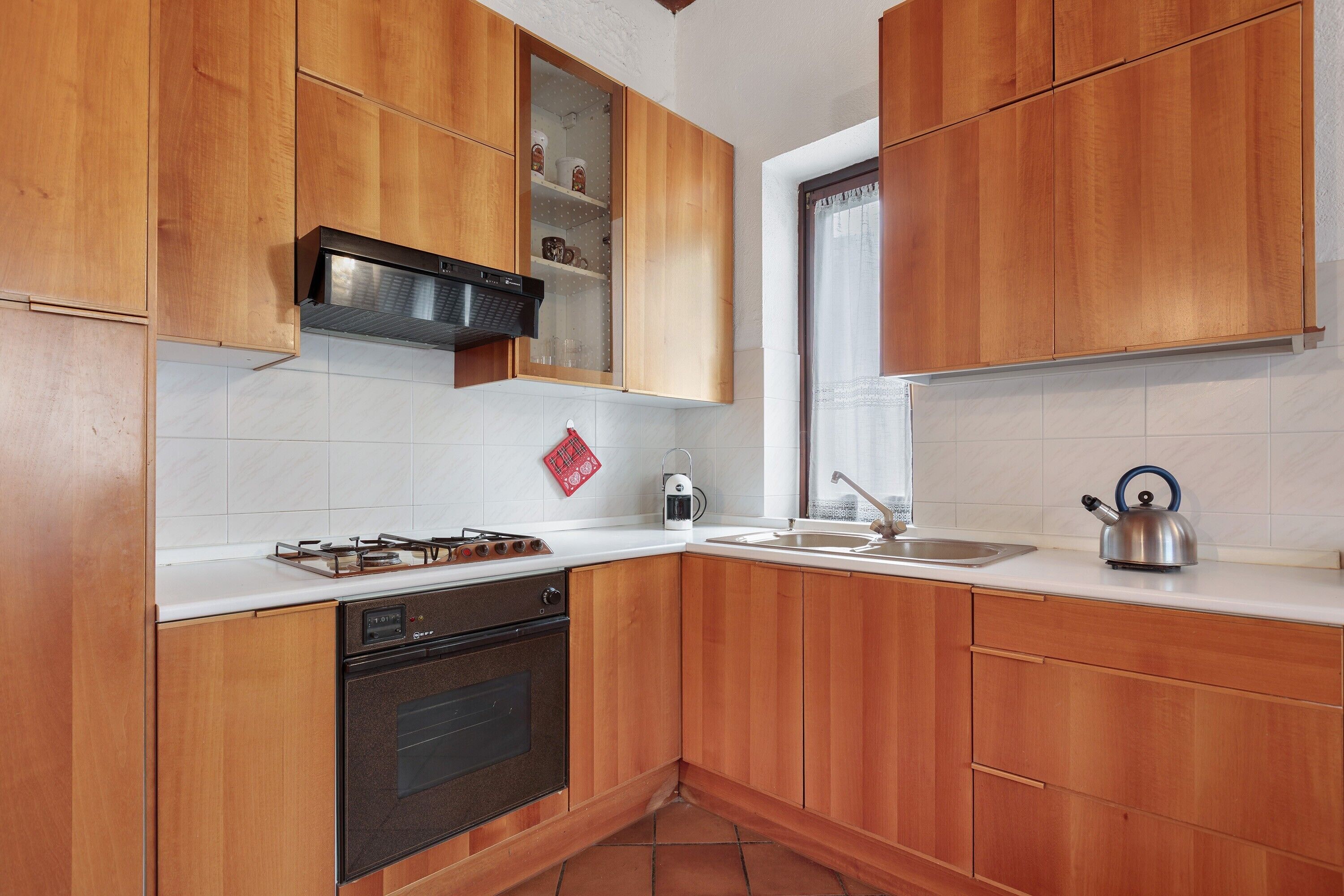 Une cuisine avec des meubles de rangement en bois, une cuisinière, un four, un évier et une bouilloire.