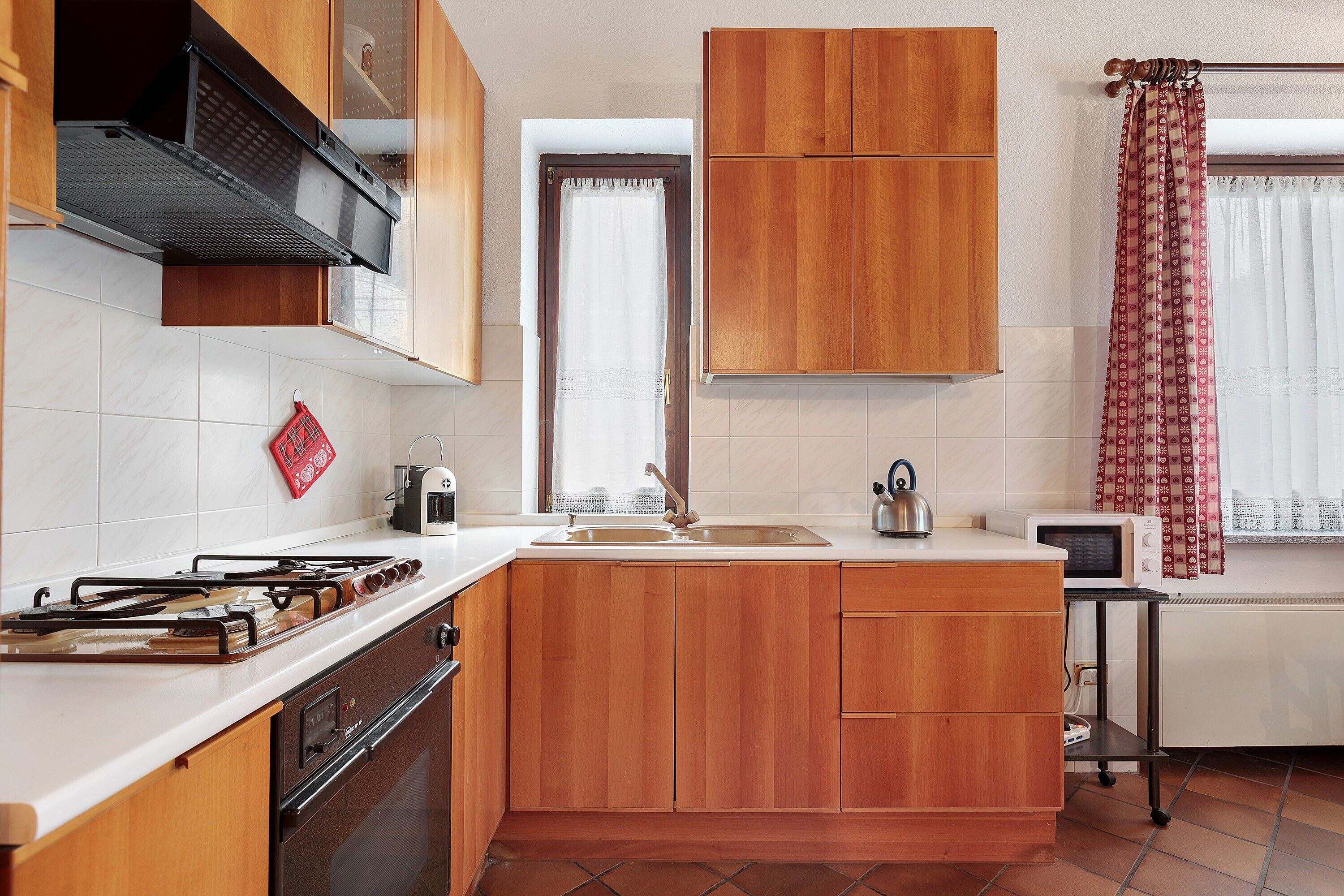 A kitchen with wooden cabinets, a gas stove, a microwave, and a window with a curtain.