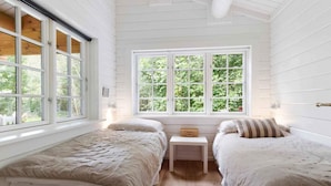Een kamer met twee bedden, een klein tafeltje en een groot raam met uitzicht op groen.