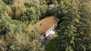 Luchtbeeld van een huis, omringd door dicht bos, met een zichtbaar terras en een groot raam.