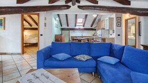 A living room with a blue sofa, wooden beams, a tiled floor, and a view into the kitchen. - Apartment 'Trilocale 13' with Mountain View and Wi-Fi (Gressan)