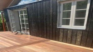 Eine Holzterrasse mit einem dunklen Holzgebäude im Hintergrund.