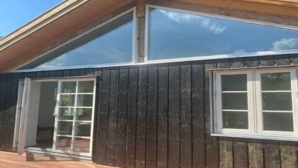 Ein modernes Haus mit einem großen Glasfenster und einer Holzterrasse.