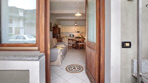 Een smalle gang die leidt naar een keuken met een eettafel, stoelen, een bank en een kleed.