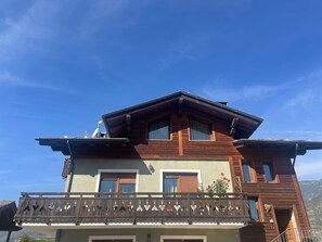 A two-story building with a wooden facade, a balcony with decorative railings, and a clear blue sky in the background.