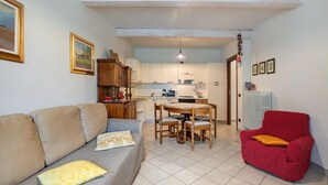 Een woonkamer met een bank, een rode fauteuil, een eettafel met stoelen en een keuken op de achtergrond.