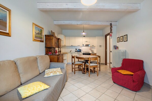 A living room with a sofa, a red armchair, a dining table with chairs, and a kitchen area in the background.